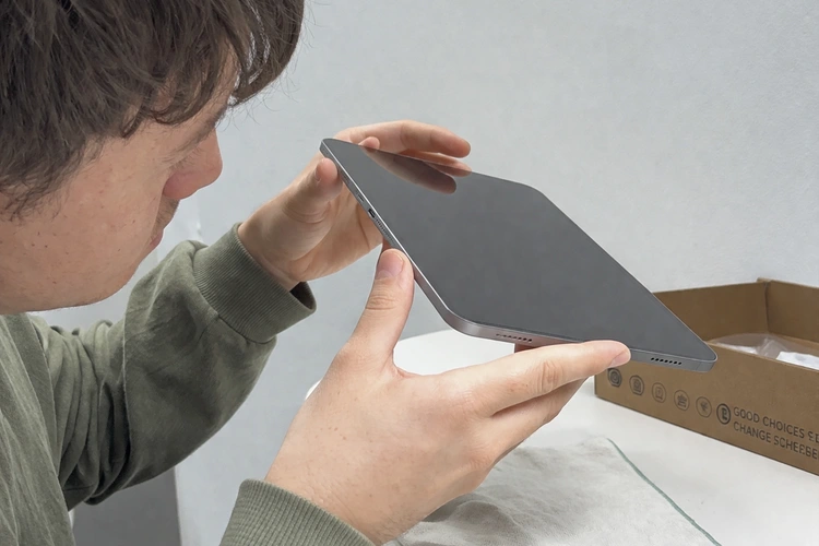 A person carefully inspecting a secondhand tablet, examining the screen and ports under bright lighting.