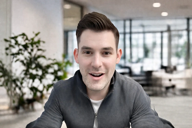 A person on a video call with a clean blurred virtual office background applied, sitting in front of a plain wall without any green screen setup visible.